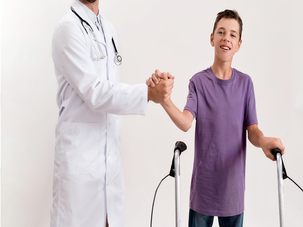 Cropped shot of male doctor shaking hands with teenaged disabled boy with cerebral palsy, taking steps using his walker isolated over white background
